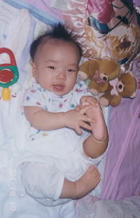 Baby Lily lay on her back in a crib. Her black hair is sticking up everywhere and she is playfully grabbing her foot.