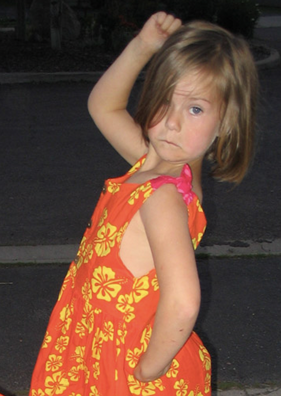 Young Grace dances very seriously in a dark room, wearing a bright orange dress with yellow hibiscus print.