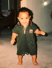 Baby Taft stands in a carpeted room smiling and walking towards the camera. He is wearing a black onesie.