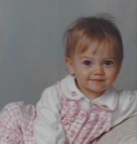 Erin as a baby lounging in a professional portrait, wearing a pink checkered jumper