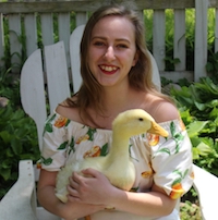 Lilli sits in a white adirondack chair and smiles while holding a duck on her lap