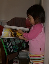 Baby Michika reads a magazine. She is wearing a pink pajama top and rainbow striped pajama pants.